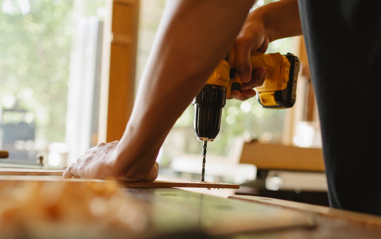 pexels-photo-5974053 Close-up of a person using a power drill on wood indoors during daytime.
