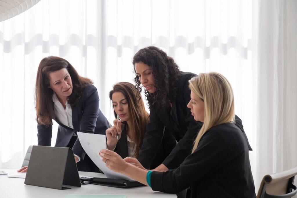 pexels-photo-8171208 Four businesswomen engaged in discussion over documents in a contemporary office setting.