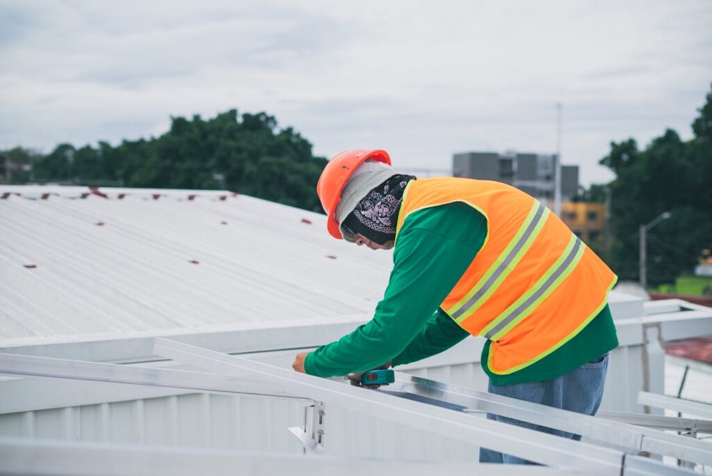 pexels-photo-8853474 A construction worker wearing safety gear working on rooftop installation outdoors.